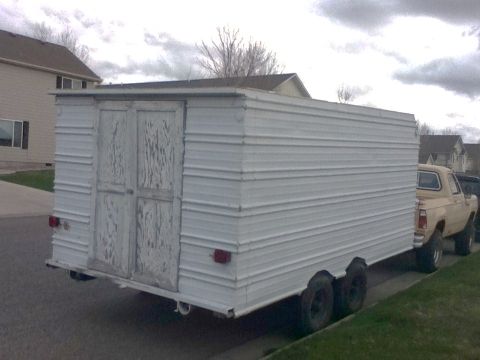 2006 Ford E350 - A white trailer with weathered double doors is towed by a tan pickup truck on a cloudy day.