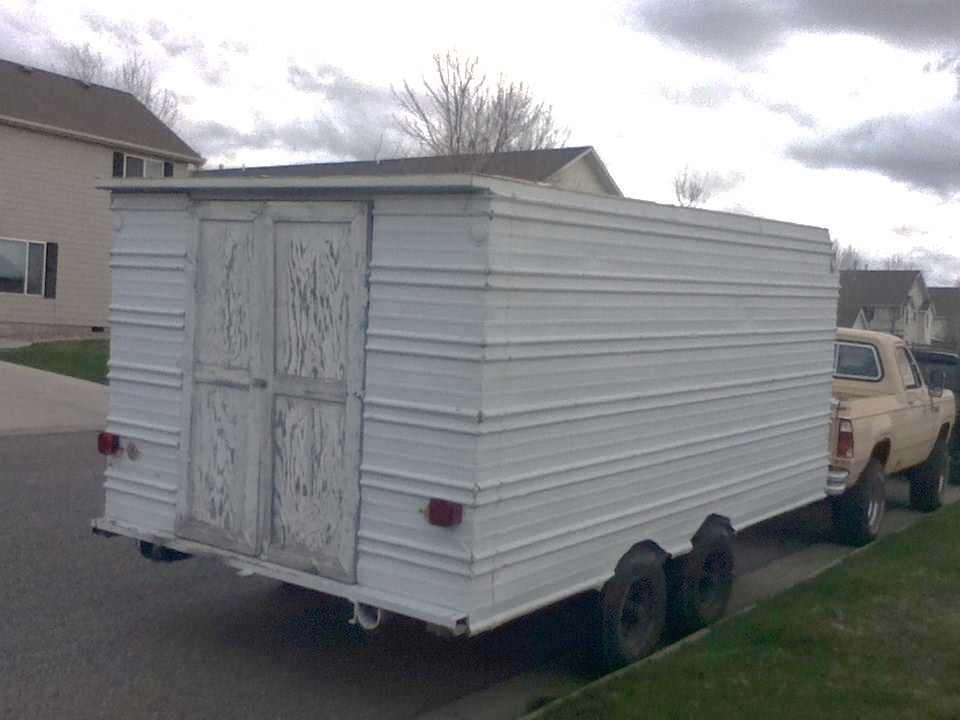White trailer with double doors, towed by a tan pickup truck, parked on a residential street