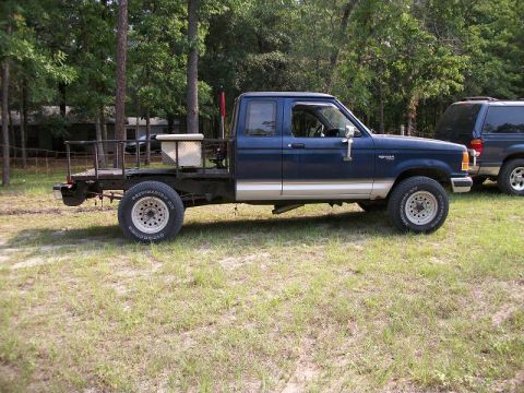 1994 Ford Explorer - A blue Ford Ranger pickup truck with a custom flatbed is parked outdoors next to an SUV.