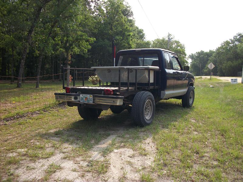Dark blue pickup truck with a flatbed, toolboxes, and dual rear wheels, viewed from the rear