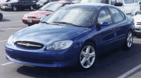 1993 Ford Taurus - A blue Ford sedan is parked in a lot with other vehicles around it.