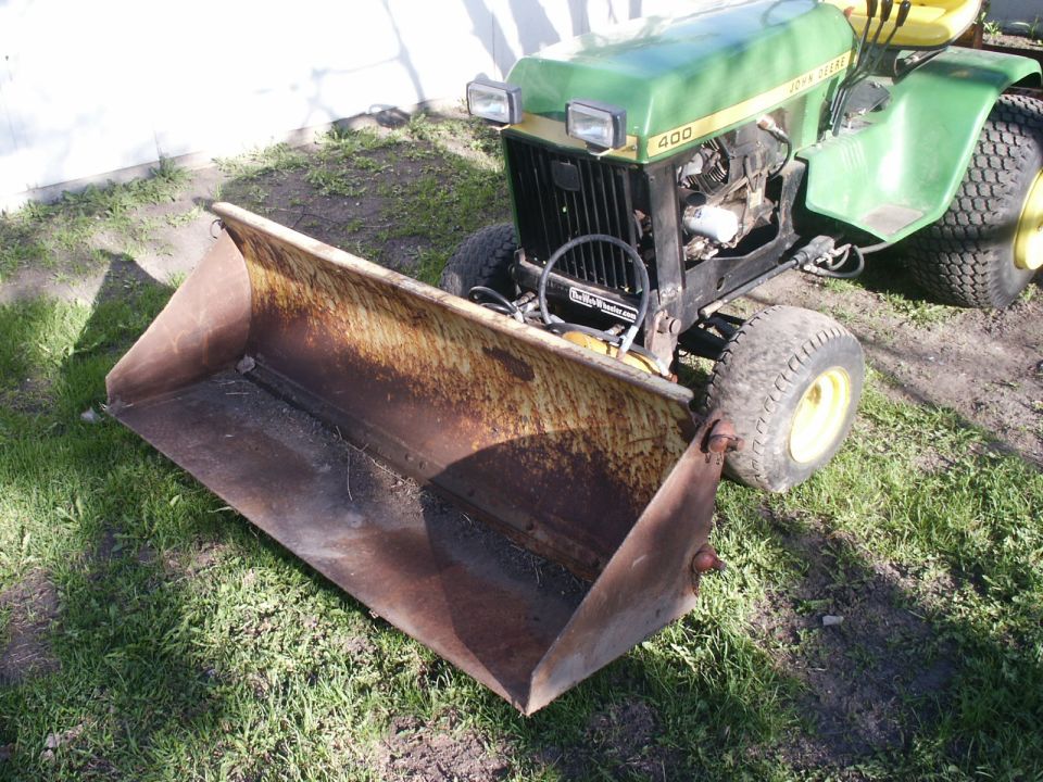 Green John Deere 400 tractor with a rusty front loader attachment parked on grass