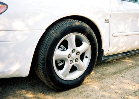 2000 Ford Taurus - A flat tire on the driver's side of a white vehicle is pictured, with a '24V' badge on the fender.