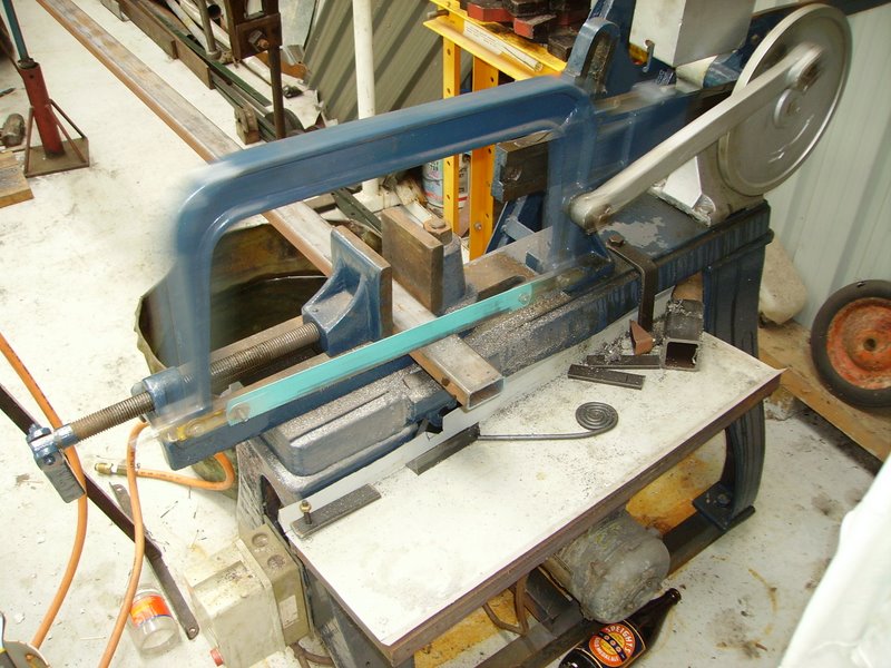Metal cutting bandsaw in a workshop with a blue frame and a metal blade