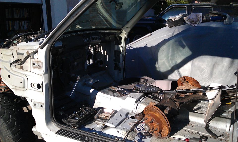 Disassembled white truck interior with exposed engine bay and rusty brake components