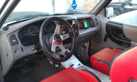 1992 Ford Ranger - The interior of a Ford Ranger shows red seats and an aftermarket steering wheel, with the radio area open.