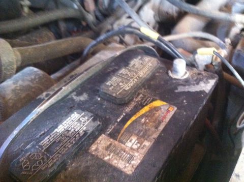 1990 Ford Bronco - Close-up view of a car battery within an engine bay, warning labels and a SuperMotors watermark.