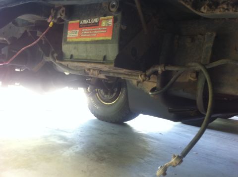 1990 Ford Bronco - Undercarriage view of a vehicle, a Kirkland battery and a tire.