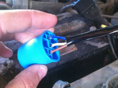 1990 Ford Bronco - A blue electrical connector with three wires is held by a hand, with a blurry engine bay in the background.