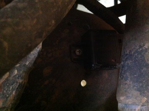 1990 Ford Bronco - Close-up of an unidentified vehicle component, showing a screw and a hole on a dark metal surface.