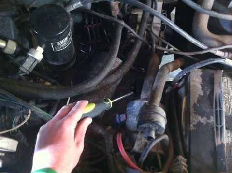 1990 Ford Bronco - Close-up of an engine bay with a hand holding a screwdriver, focusing on various mechanical parts and wiring.