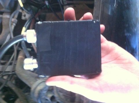 1990 Ford Bronco - A black box with fittings is held in a hand, with engine parts visible behind it.