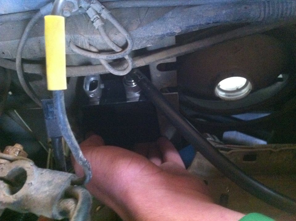 Undercarriage of a vehicle with a hand reaching towards a metal component and hoses