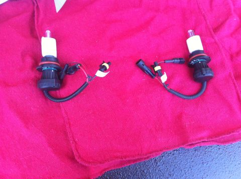 1990 Ford Bronco - Two automotive headlight bulbs with wiring are displayed on a red cloth, with a Supermotors watermark visible.