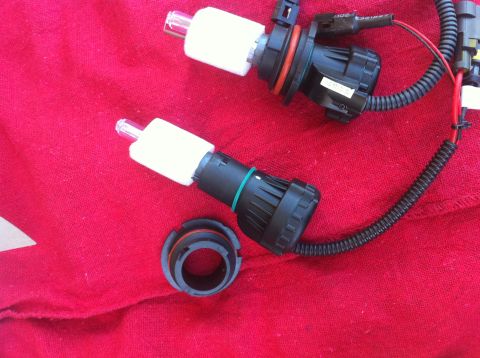 1990 Ford Bronco - Two HID headlight bulbs and a mounting ring are shown on a red fabric background.