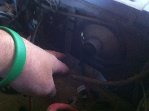1990 Ford Bronco - A hand with a green bracelet is seen in a dark engine bay, with a fan visible in the background.