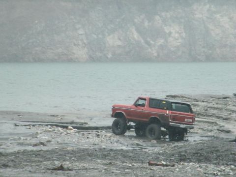 1978 Ford Bronco - Red 1978 Ford Bronco navigates a rough, wet terrain near a large body of water.