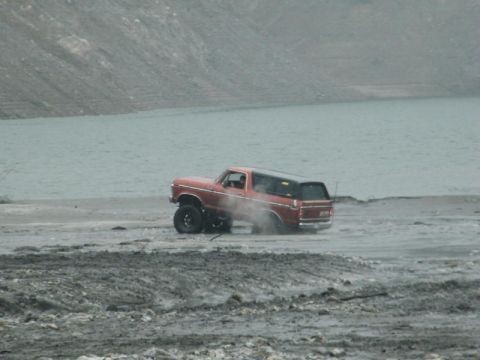 1978 Ford Bronco - A red 1978 Ford Bronco navigates a dusty, off-road terrain with a large body of water in the background.