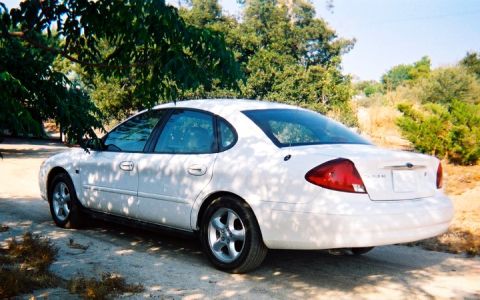 2000 Ford Taurus - A white 2000 Ford Taurus sedan is parked outdoors, with trees and foliage in the background.