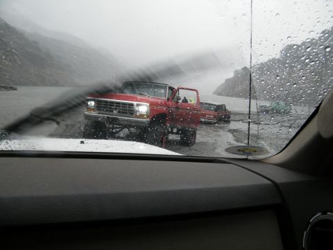 1978 Ford Bronco - Two red Ford trucks drive through the rain on a wet road.