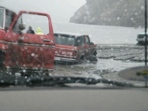 1978 Ford Bronco - Two vehicles are stuck in thick mud near a body of water, with a third vehicle visible in the distance.