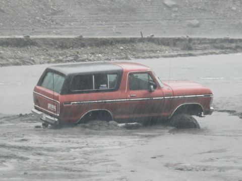 1978 Ford Bronco - A red 1978 Ford Bronco is stuck in muddy terrain, with its wheels partially submerged.