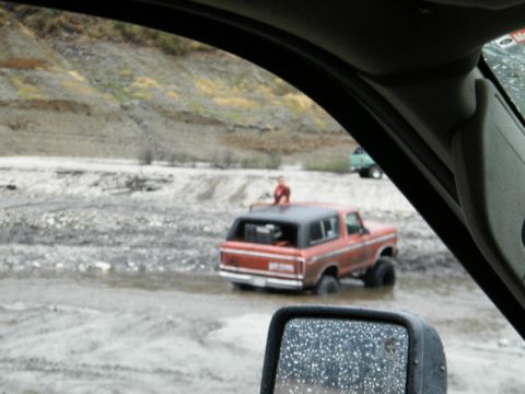 1978 Ford Bronco - A red 1978 Ford Bronco navigates through a muddy, watery terrain, with another vehicle visible in the background.
