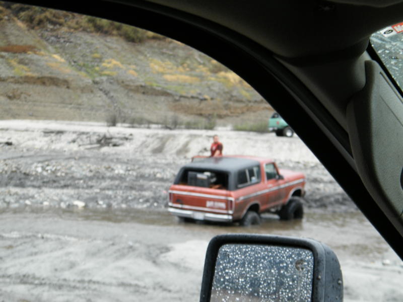 Red 1978 Ford Bronco driving through muddy water, rear view