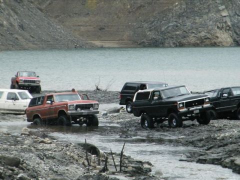 1978 Ford Bronco - Several SUVs, including a 1978 Ford Bronco, navigate a muddy, watery terrain.
