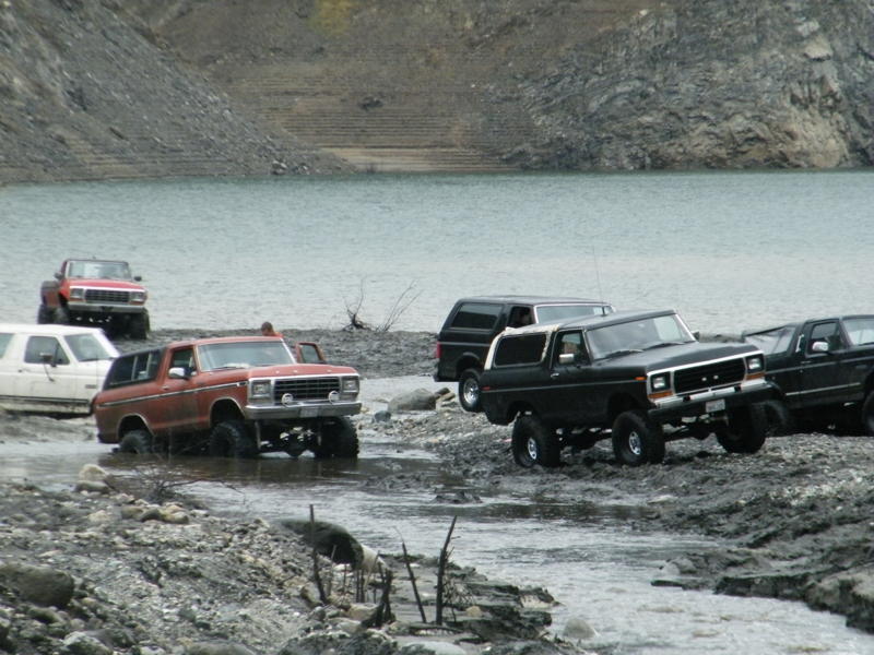 1978 Ford Bronco and other SUVs driving through shallow water and mud