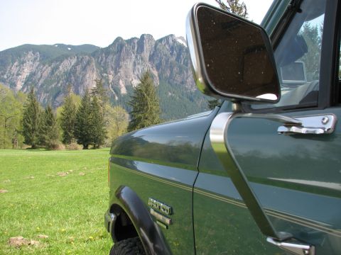 1990 Ford Bronco - Side view of a green 1990 Ford Bronco parked in a grassy field with mountains in the background.