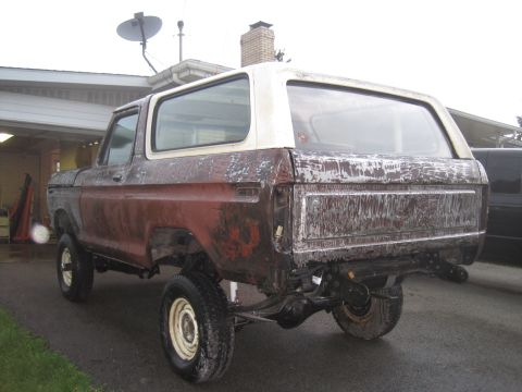 1979 Ford Bronco - Rear view of a 1979 Ford Bronco with a weathered red and white body, showing its off-road tires and suspension.