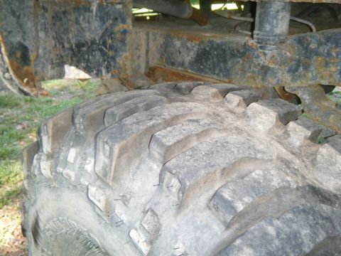 1990 Ford Bronco - A close-up view of a large, off-road tire and the rusty undercarriage of a vehicle.