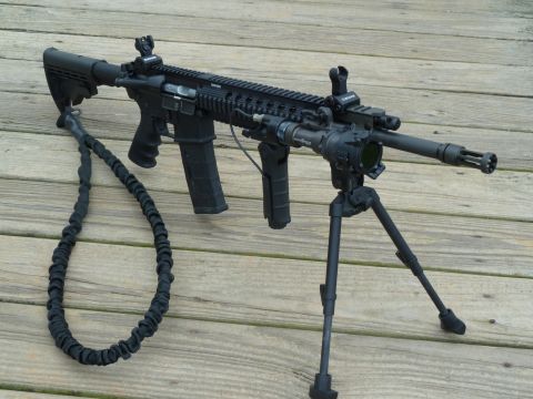 1992 Ford Mustang - An assault rifle with tactical accessories is displayed on a wooden surface.