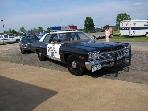 1991 Ford Crown Victoria - A vintage police car is parked outdoors with other vehicles and a person standing nearby.