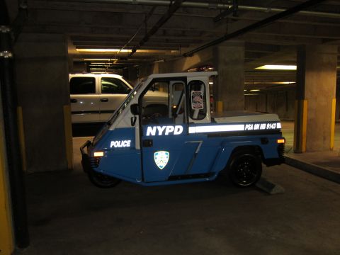 1991 Ford LTD Crown Victoria - blue-and-white three-wheeled 'NYPD POLICE' scooter parked in a concrete garage beside a pickup truck.