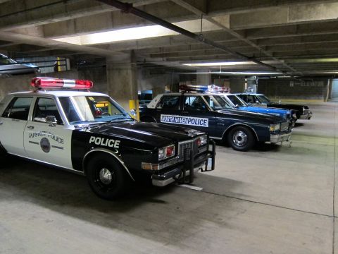 1991 Ford LTD Crown Victoria - Several black-and-white police cruisers, including a 'JAFFREY POLICE' and 'NORTH HAVEN POLICE' car, lined up in a garage.