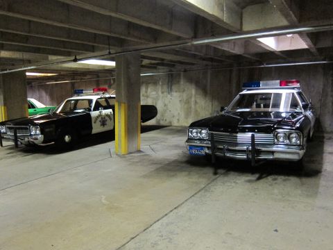 1991 Ford LTD Crown Victoria - Two black-and-white vintage highway patrol sedans with roof light bars parked in a concrete parking structure.
