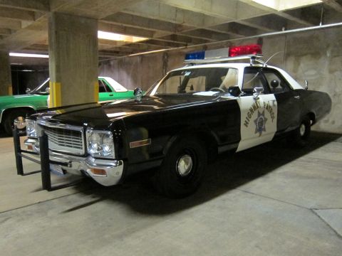 1991 Ford LTD Crown Victoria - black-and-white Highway Patrol sedan with a front push bar and roof light bar parked in a dim concrete garage beside a green car.