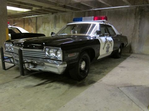 1991 Ford LTD Crown Victoria - black-and-white Dodge Highway Patrol sedan with a front push bar and roof light bar parked in a dim concrete garage.