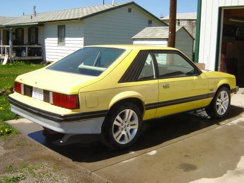 1979 Ford Mustang - A yellow 1979 Ford Mustang coupe is parked on a concrete driveway in front of a house.