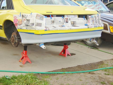 1979 Ford Mustang - The rear of a yellow vehicle is elevated on red jack stands, revealing its undercarriage and exhaust system.