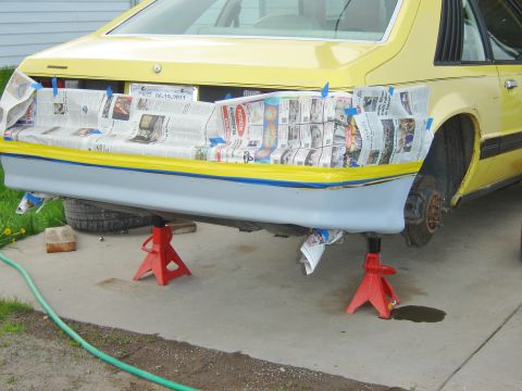 1979 Ford Mustang - The rear of a yellow car with racing numbers is visible, elevated on jack stands.