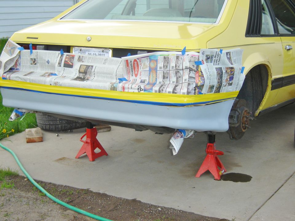 Yellow car body with racing numbers on rear, raised on red jack stands