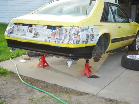 1979 Ford Mustang - A yellow van is elevated on jack stands for maintenance, with one wheel removed.