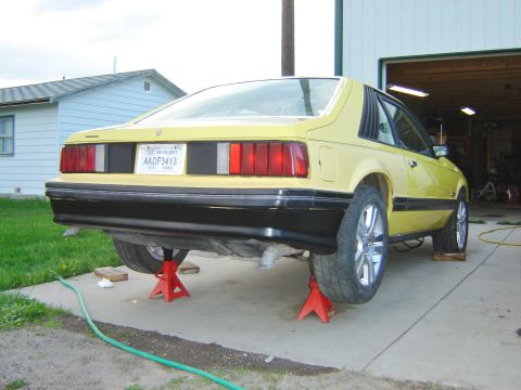 1979 Ford Mustang - Rear view of a yellow pickup truck, elevated on jack stands for maintenance.