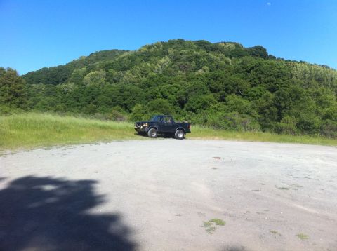 1990 Ford Bronco - A black pickup truck sits in a gravel lot under a clear blue sky with a large, tree-covered hill in the background.