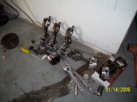1995 Ford Probe - Engine parts, including pistons and connecting rods, lie on a concrete floor next to various tools.