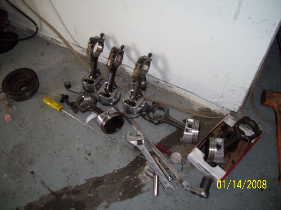 Pistons and connecting rods scattered on garage floor with tools