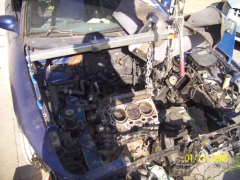 1995 Ford Probe - Engine removed from blue car, crane hook suspended over the engine bay.